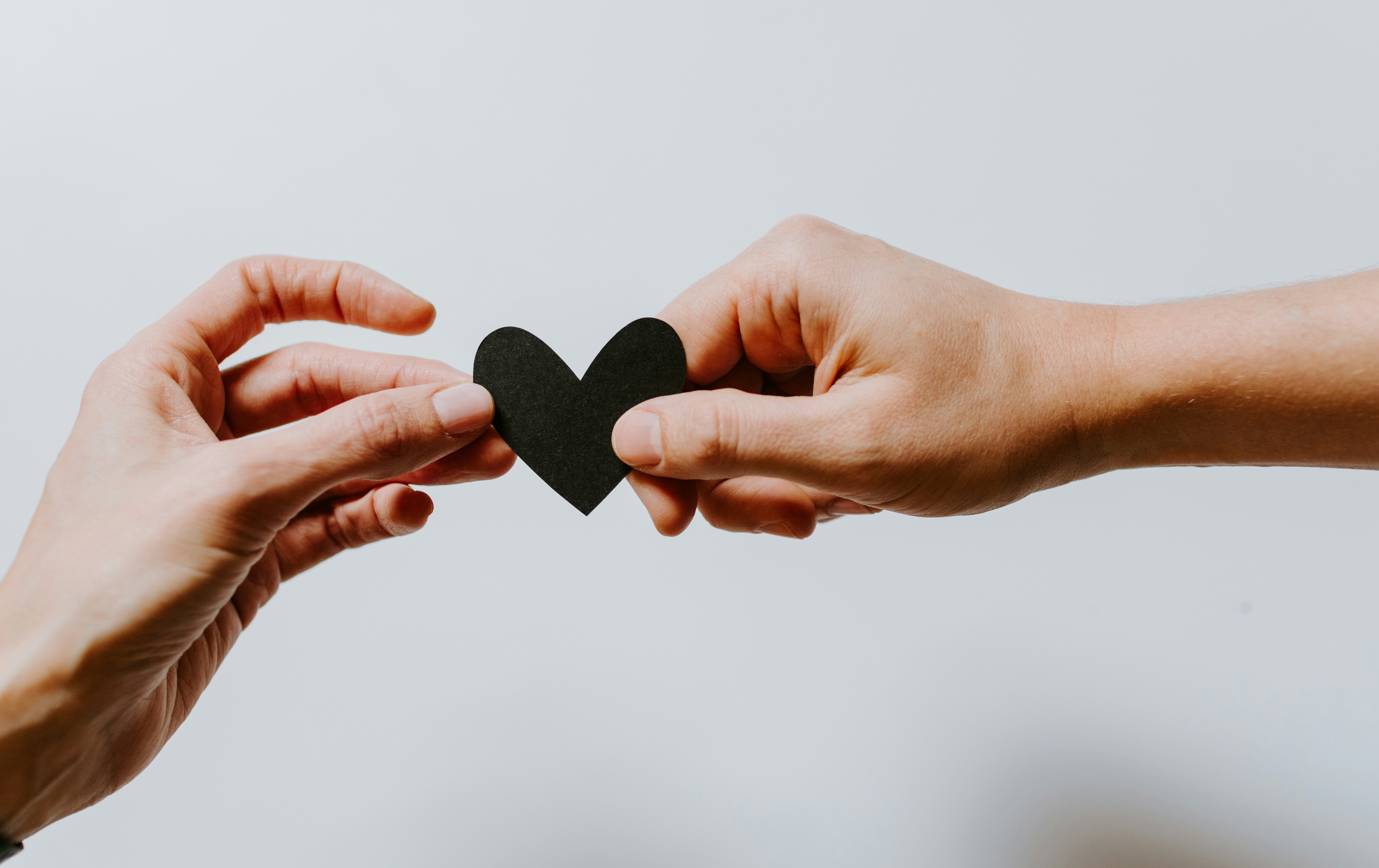 Two hands holding a small black paper heart on a white background.